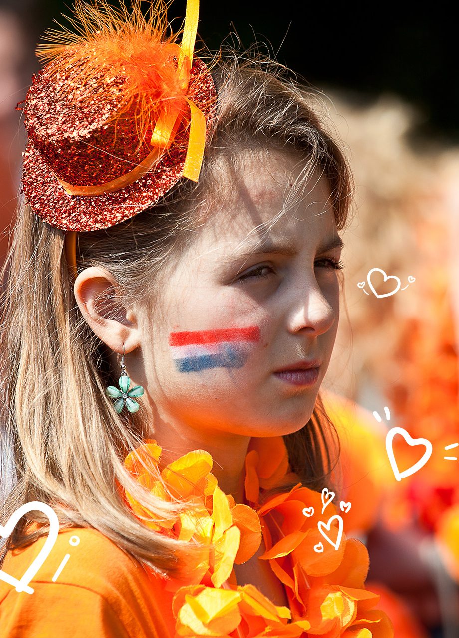 Meisje gekleed in het oranje met Nederlandse vlag op haar wang en getekende doedels in de afbeelding.