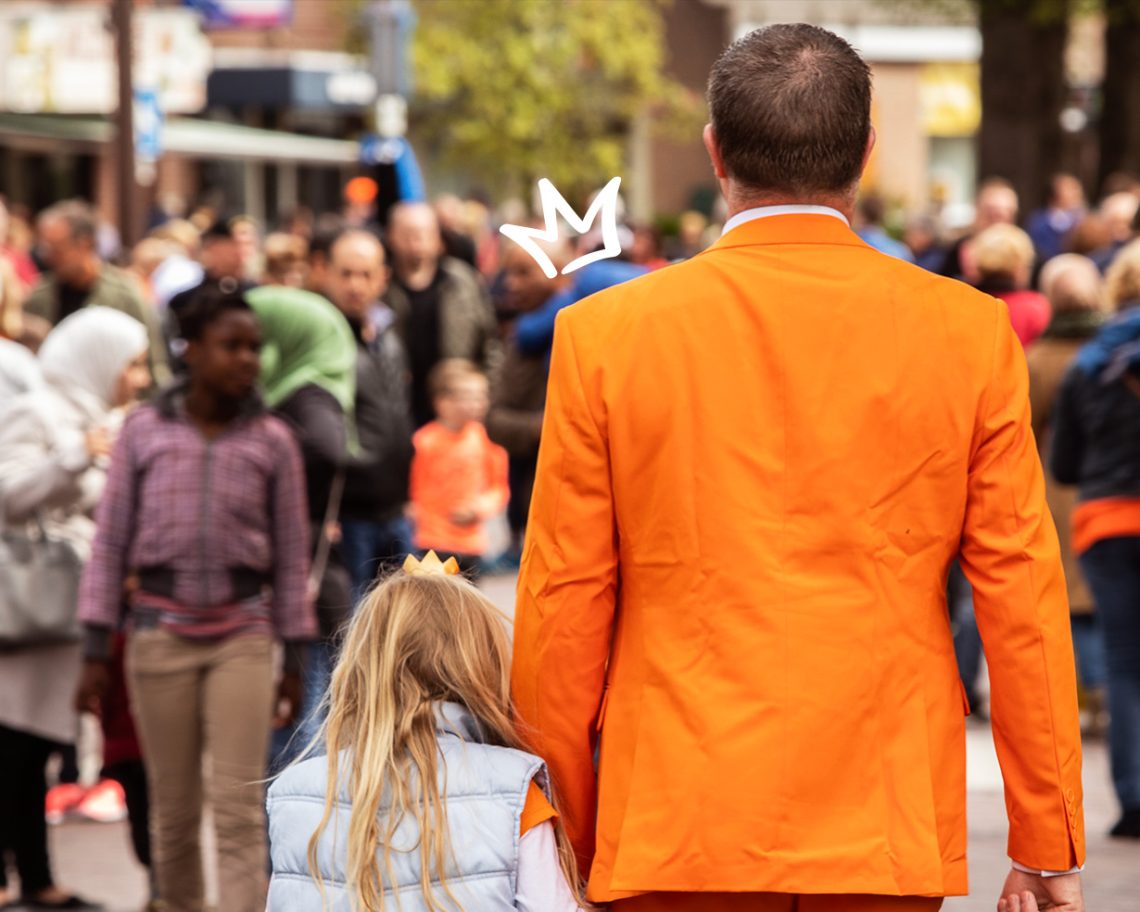 Een man loopt met kind in oranje kleding door een drukke straat.