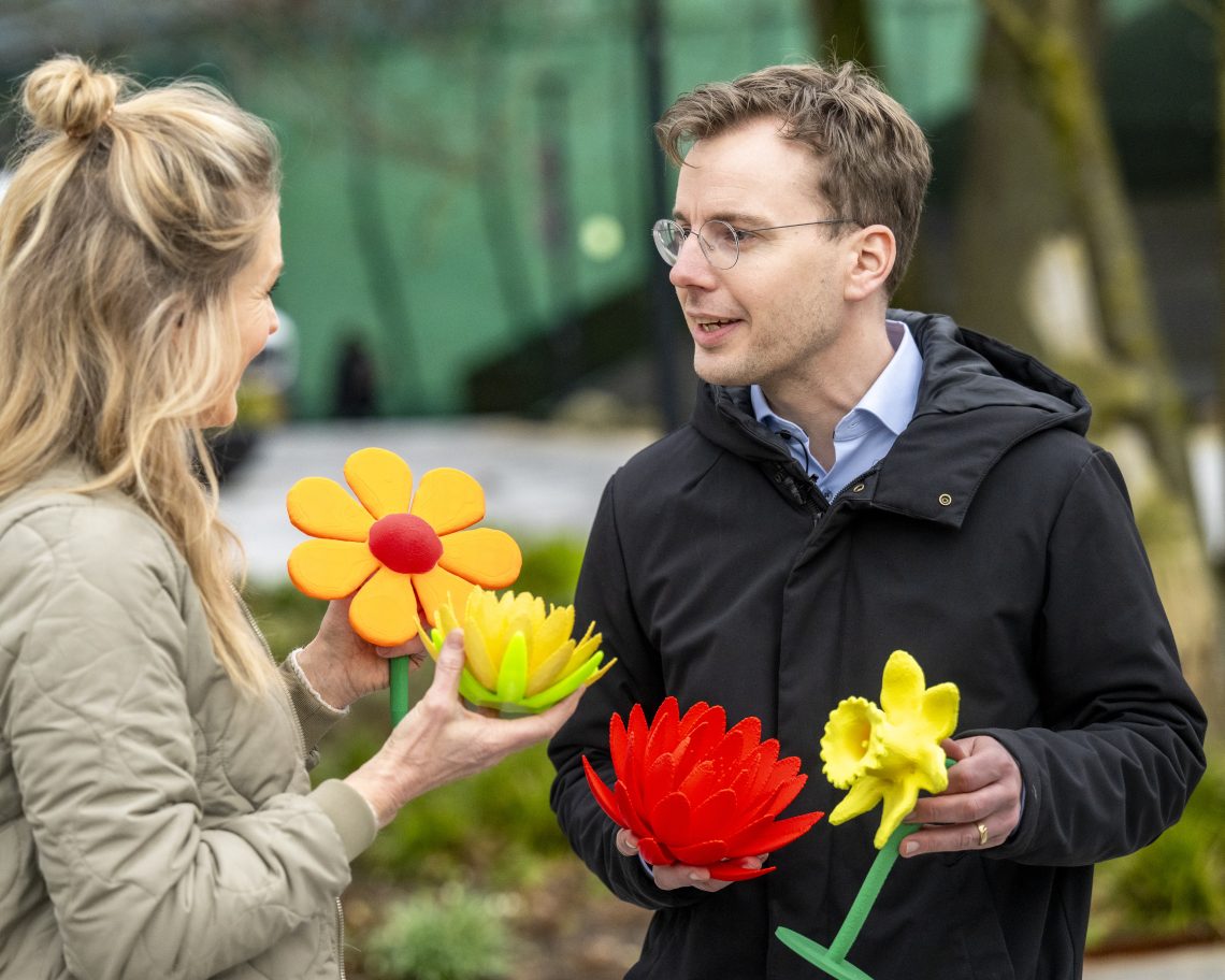 Presentatrice Margreet Beetsma met een man voor het gemeentehuis en bloemen in hun hand.