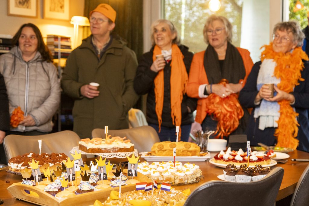 Mensen vieren in oranje kleding Koningsdag met zelfgemaakte baksels
