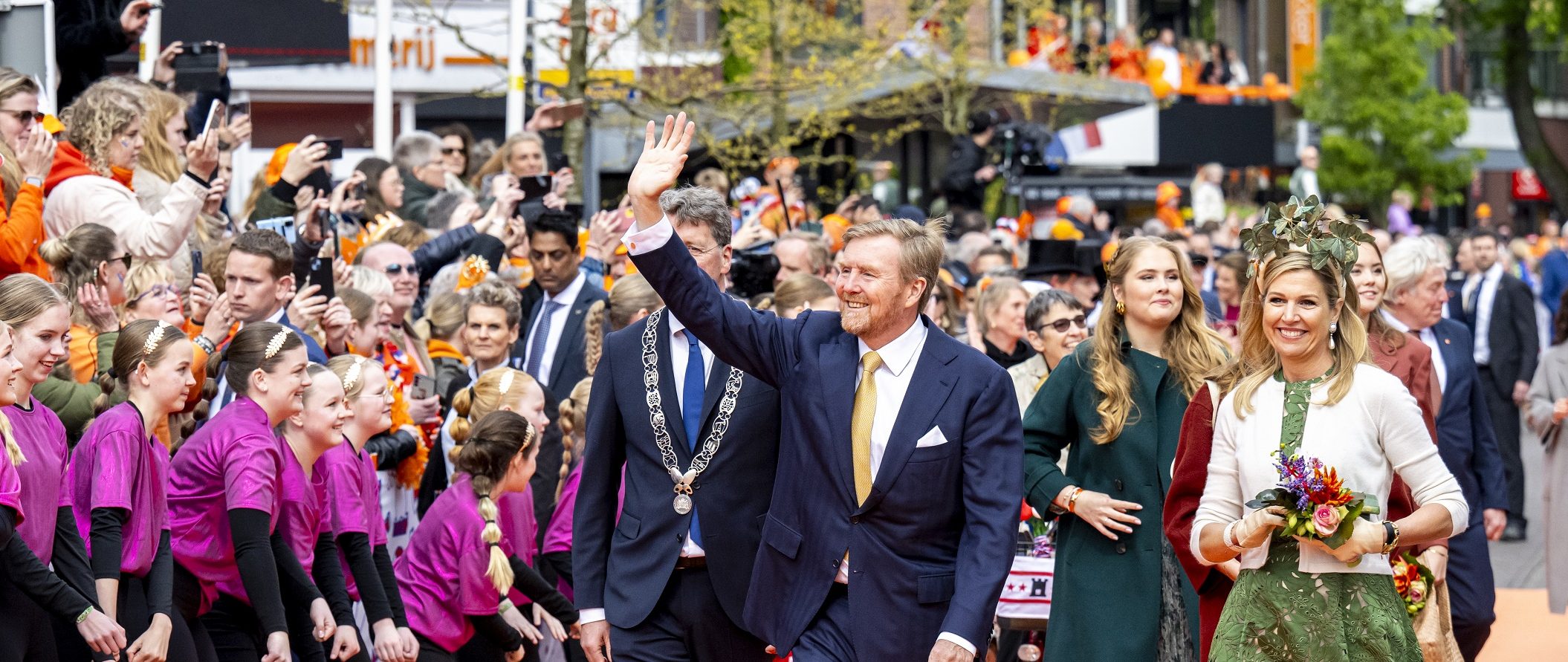 Koninklijke familie loopt over oranje loper langs de dansers.