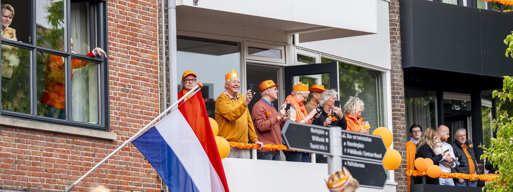 Meerdere bewoners op een balkon langs de route tijdens Koningsdag in Emmen.